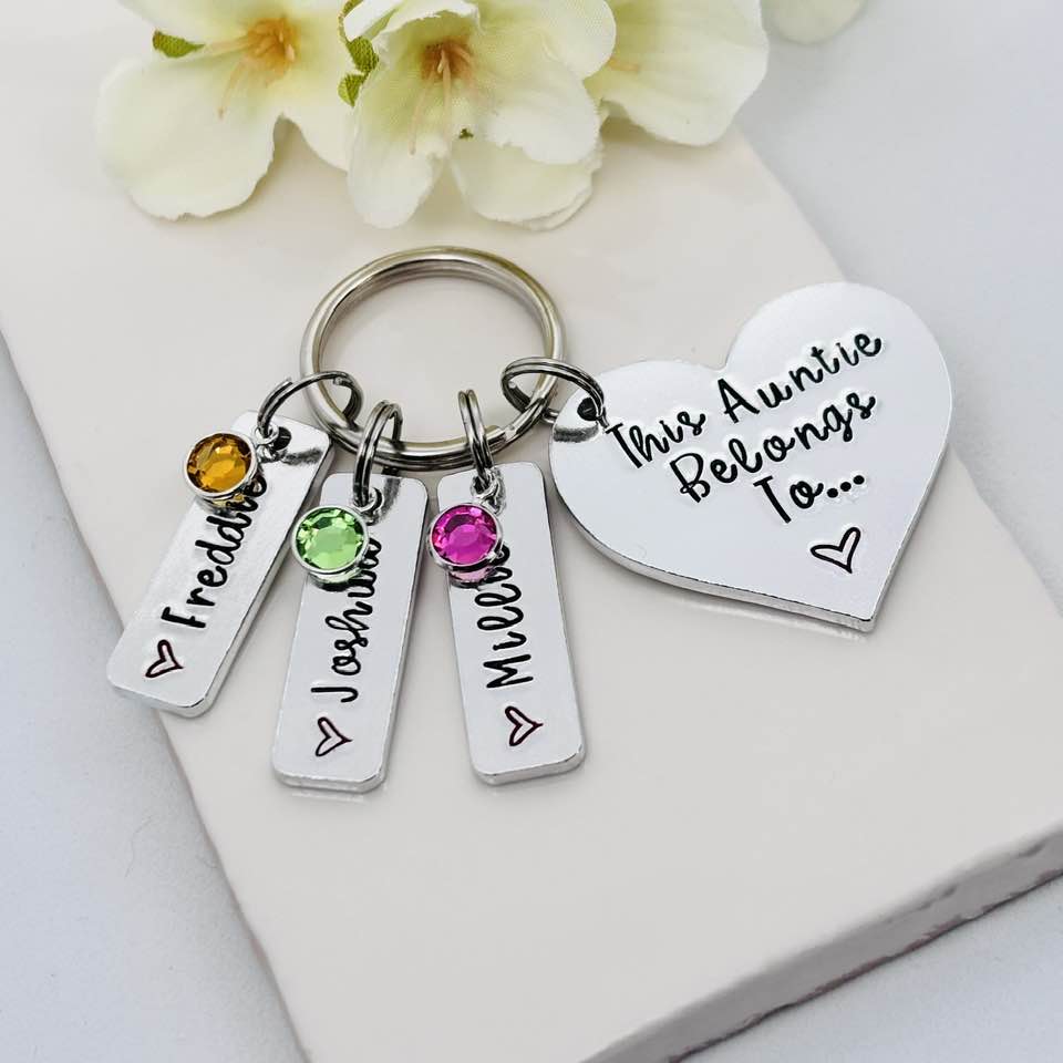 Personalised Auntie heart keyring with three name tags and colourful birthstone charms, displayed with pale flowers behind

