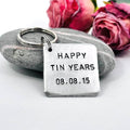 Square aluminium Happy Tin Years keyring with the personalised date 08.08.15, displayed against a grey stone with pink roses
