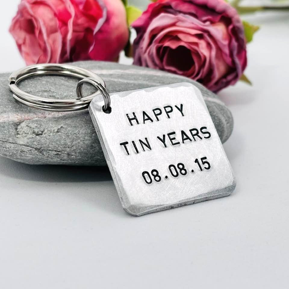 Angled view of an aluminium Happy Tin Years anniversary keyring with a personalised date, beside pink roses
