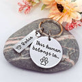 Personalised This Human Belongs To keyring with a round paw print tag and rectangular Bodie name tag, displayed on a striped stone
