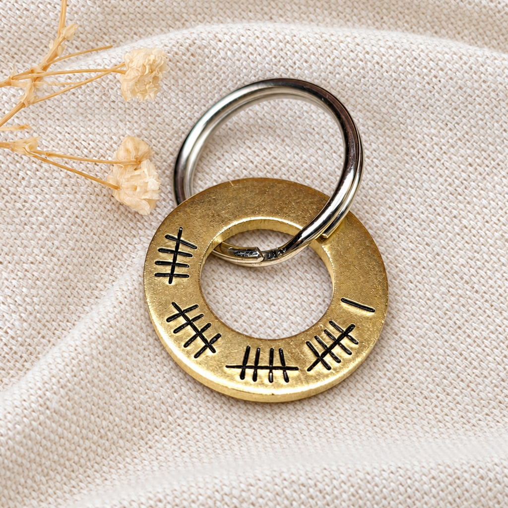 Brass 21st anniversary washer keyring with 21 hand stamped tally marks, displayed on linen beside dried flowers
