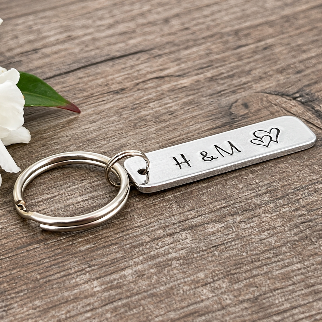 Angled close-up of a hand-stamped initial bar keyring with overlapping hearts on a wooden surface

