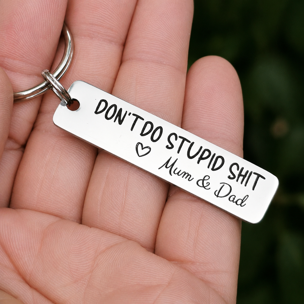 Personalised Don't Do Stupid Shit keyring with Mum & Dad signature and an outline heart, held in a hand