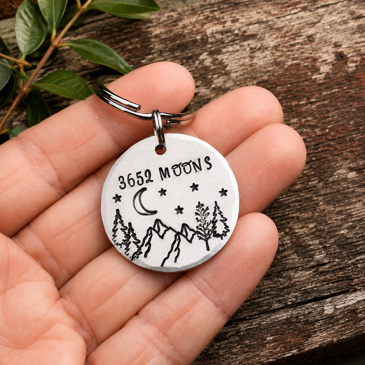 3652 Moons aluminium anniversary keyring held in a hand, showing the mountain and night-sky design
