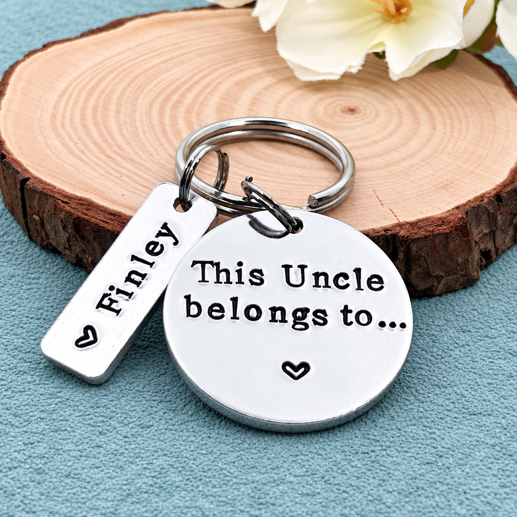 A silver metal keychain with a round disc engraved with 'This Uncle belongs to.