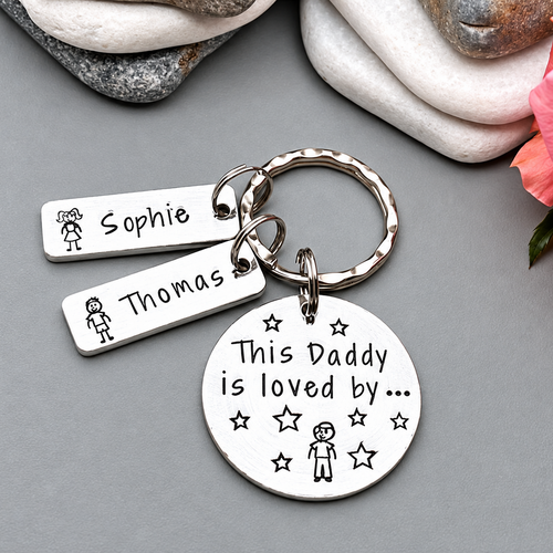 Personalized silver metal keychain with a round disc and two rectangular tags engraved with names and the phrase 'This Daddy is loved by.