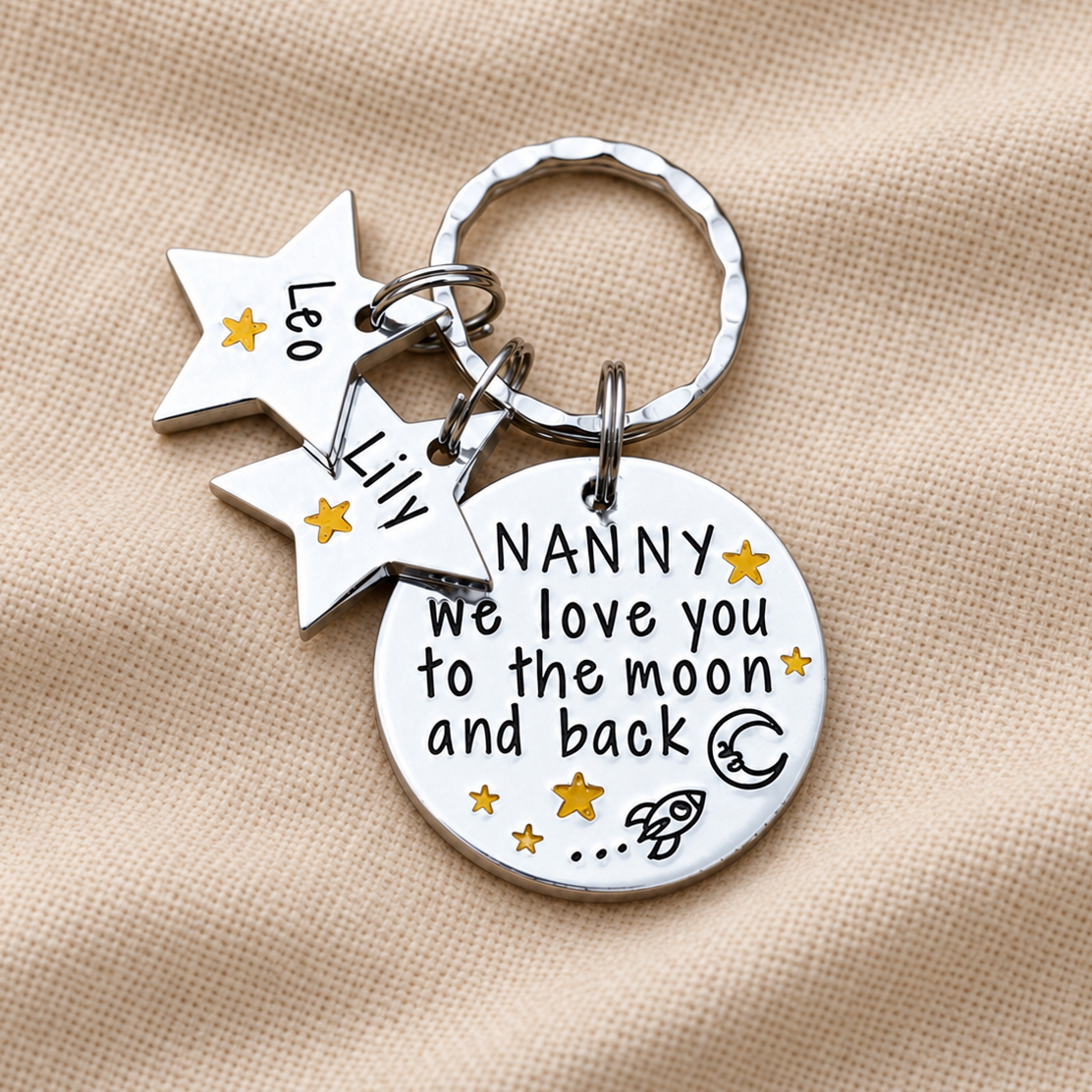Close-up of a Nanny moon and back keyring with Leo and Lily star name tags, gold-coloured stars and a rocket design