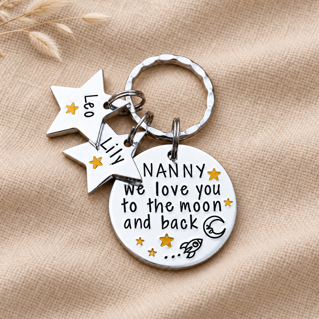 Personalised Nanny moon and back keyring with two star name tags, displayed on woven fabric beside dried stems