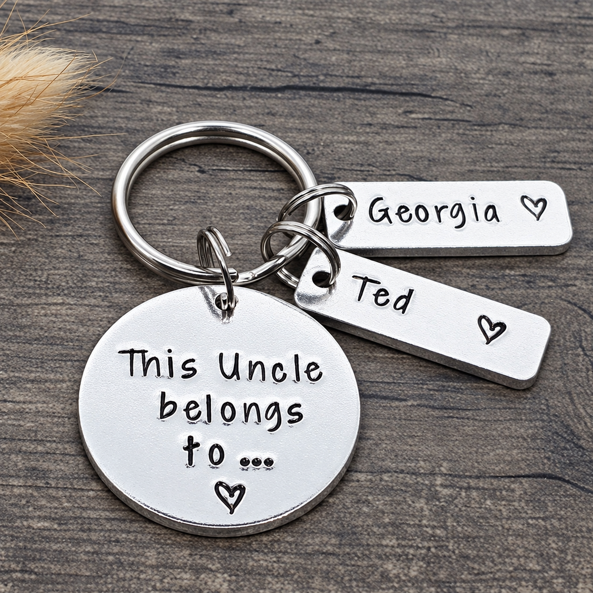 A silver metal keychain with a round disc charm and two rectangular tags, one stamped with 'Georgia' and the other with 'Ted', plus the main tag reading 'This Uncle belongs to.