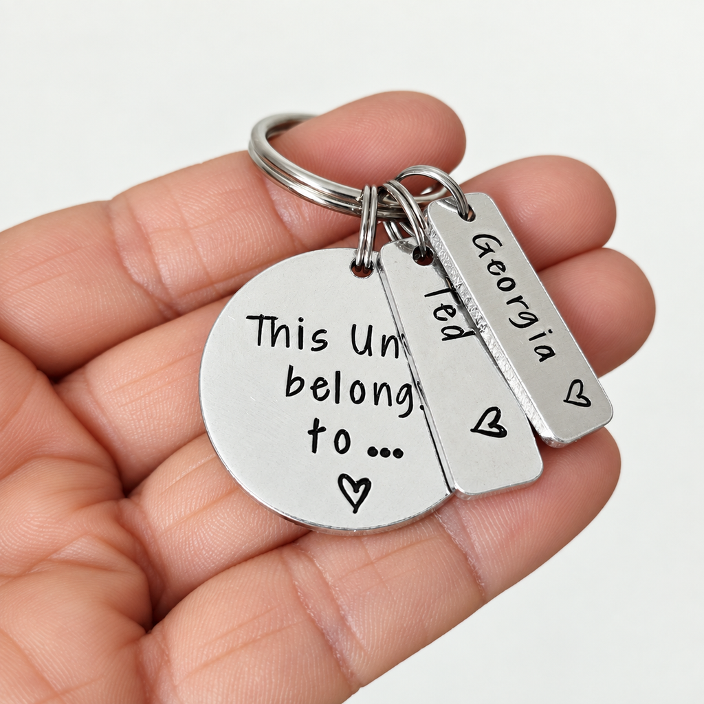 A close-up of a hand holding a silver metal keychain with two stamped pieces that form a whole message, plus a small tag reading Georgia. The hand is shown against a plain light background.