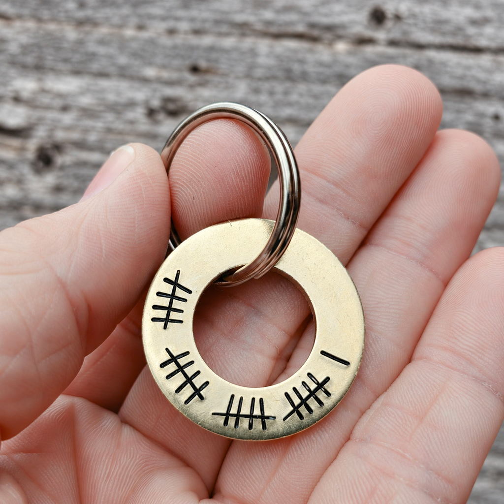 Brass washer keyring held in a hand, showing 21 tally marks around the open-centred tag
