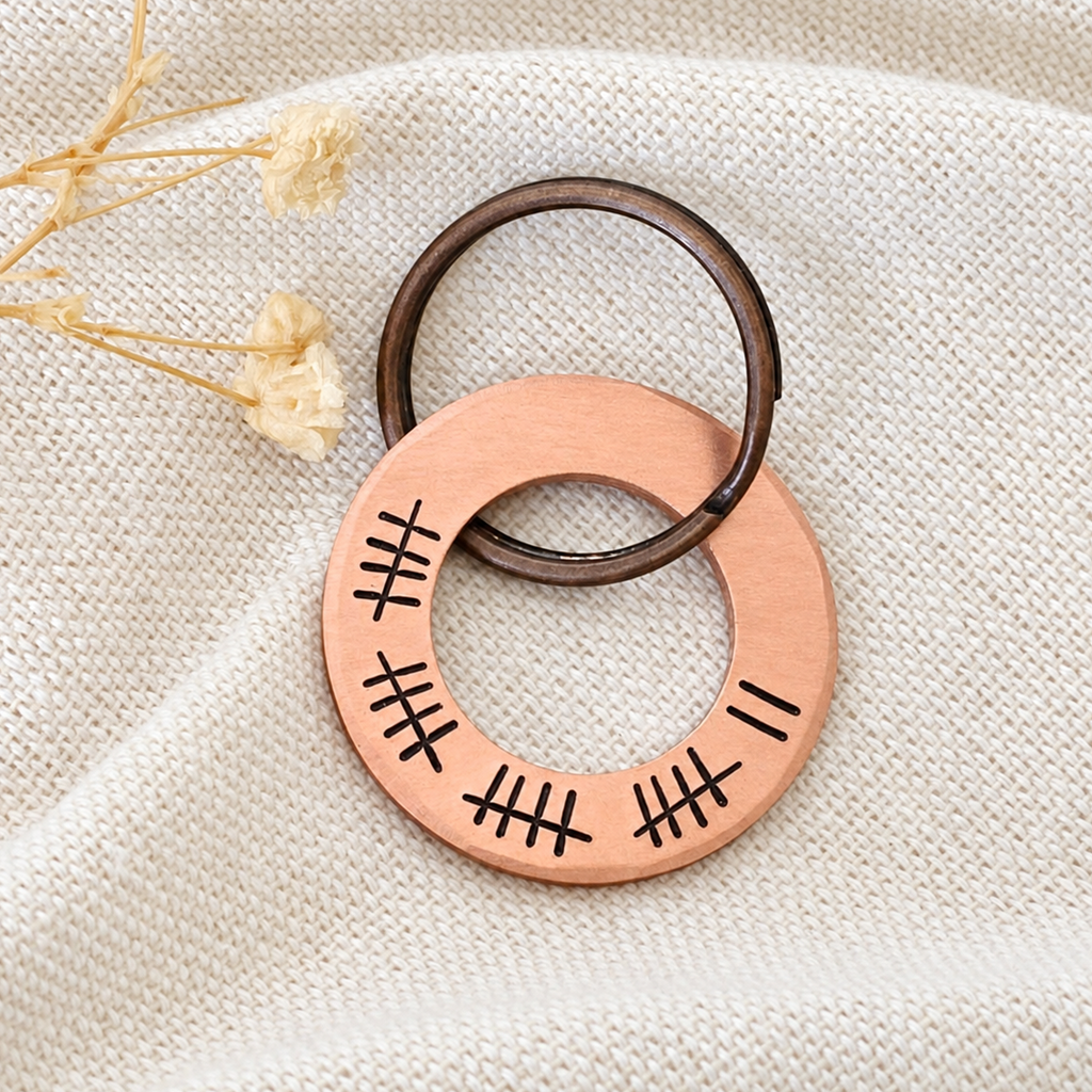 Copper 22nd anniversary washer keyring with 22 tally marks, displayed on linen fabric beside dried flowers
