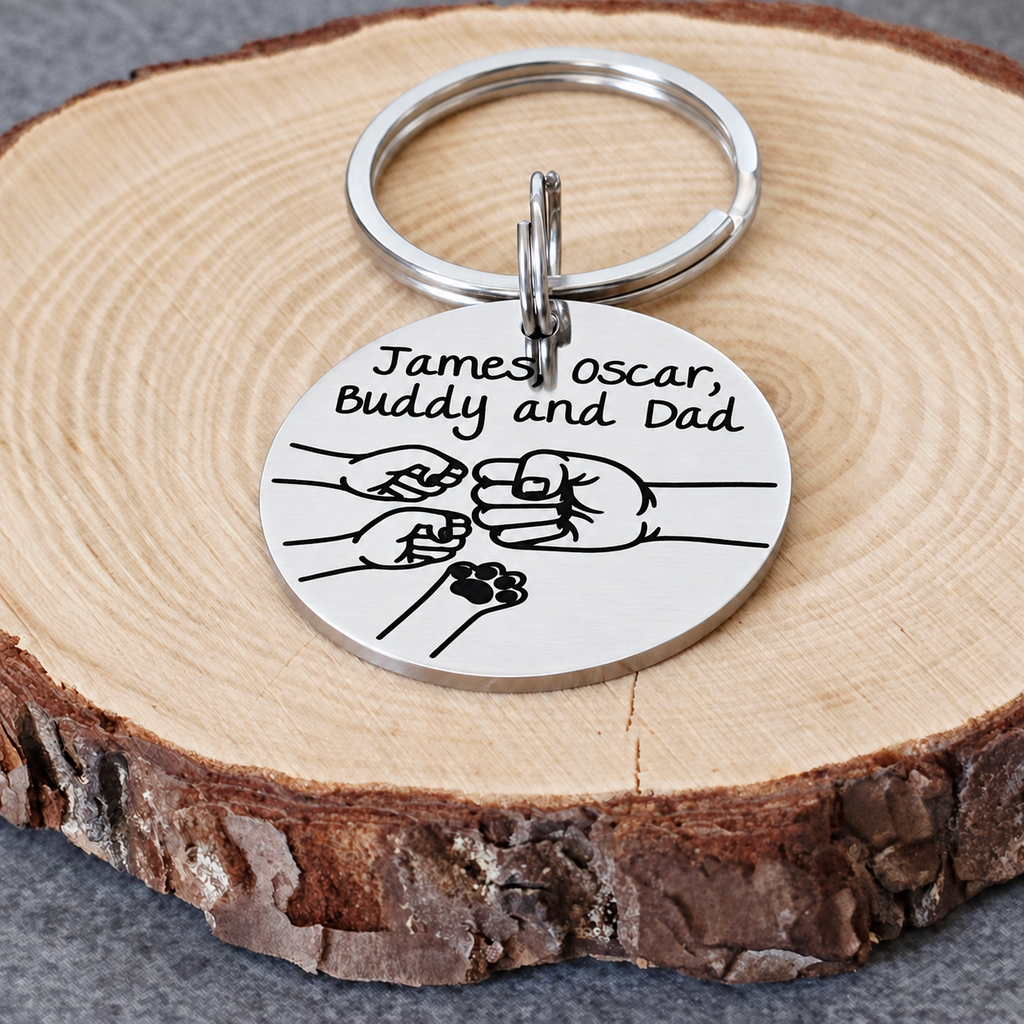 Stainless steel Dad keyring with engraved family names, fist bump design and a pet paw, resting on a wood slice

