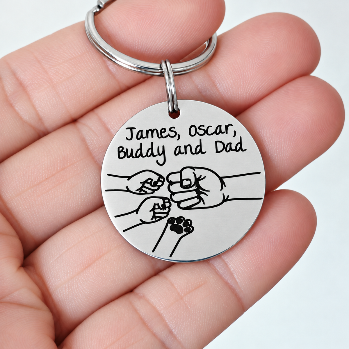Round Dad fist bump keyring engraved with James, Oscar and Buddy, held in a hand
