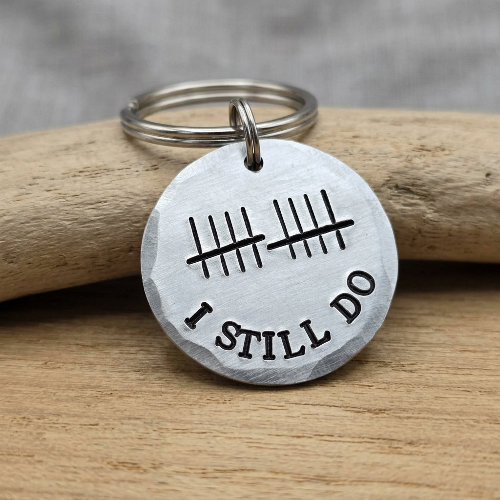Round aluminium I Still Do keyring with ten tally marks and curved lettering, displayed against smooth wood
