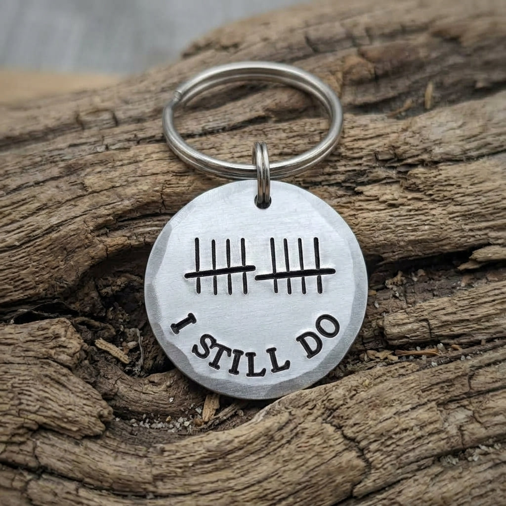 Aluminium 10th anniversary keyring with ten tally marks above curved I Still Do wording, resting on textured wood
