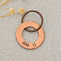 Copper washer keyring with seven hand stamped tally marks and a dark split ring, displayed on textured fabric beside dried flowers
