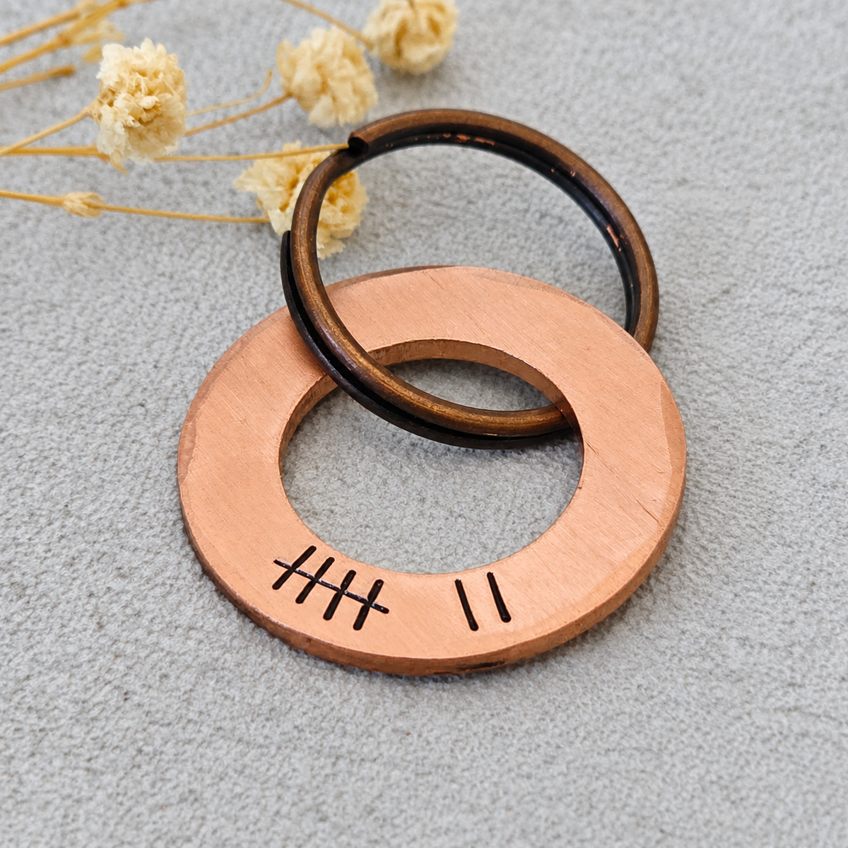 Angled close-up of a copper washer keyring showing seven tally marks, a brushed finish and a dark split ring

