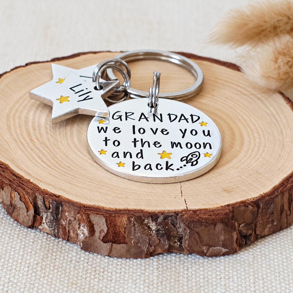 Angled view of an aluminium Grandad Moon and Back keyring with yellow stars, a rocket and star name tags
