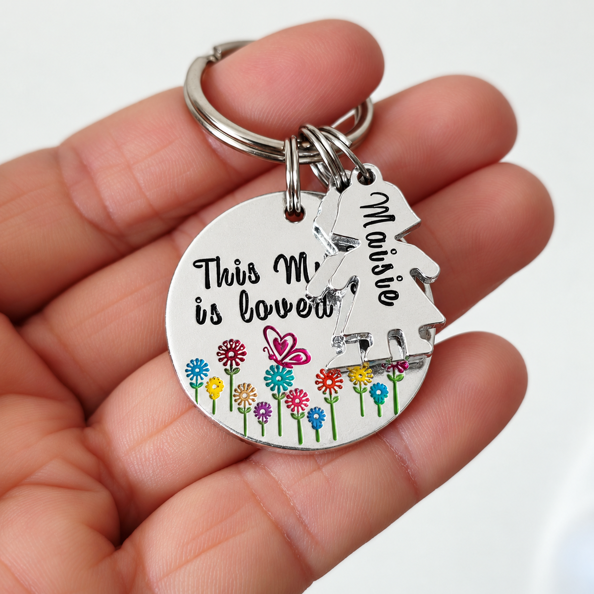 Mummy little people keyring resting on a hand, showing its colourful floral design and personalised Maisie charm
