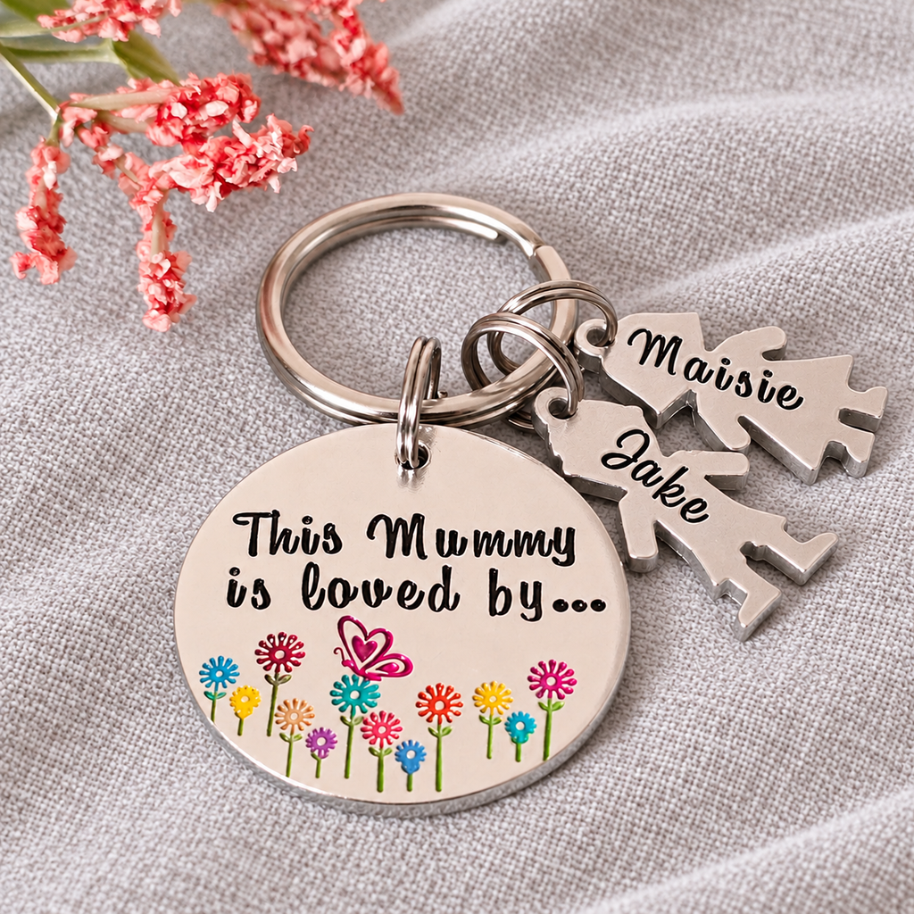 Floral This Mummy Is Loved By keyring with named girl and boy charms, displayed on linen beside pink flowers
