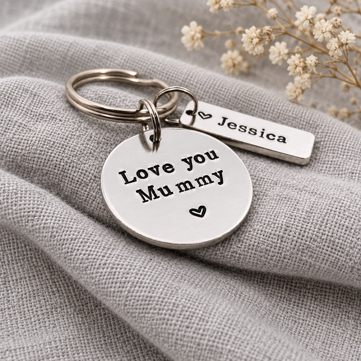 Love you Mummy round keyring with heart details and a Jessica name tag, photographed at an angle on linen fabric