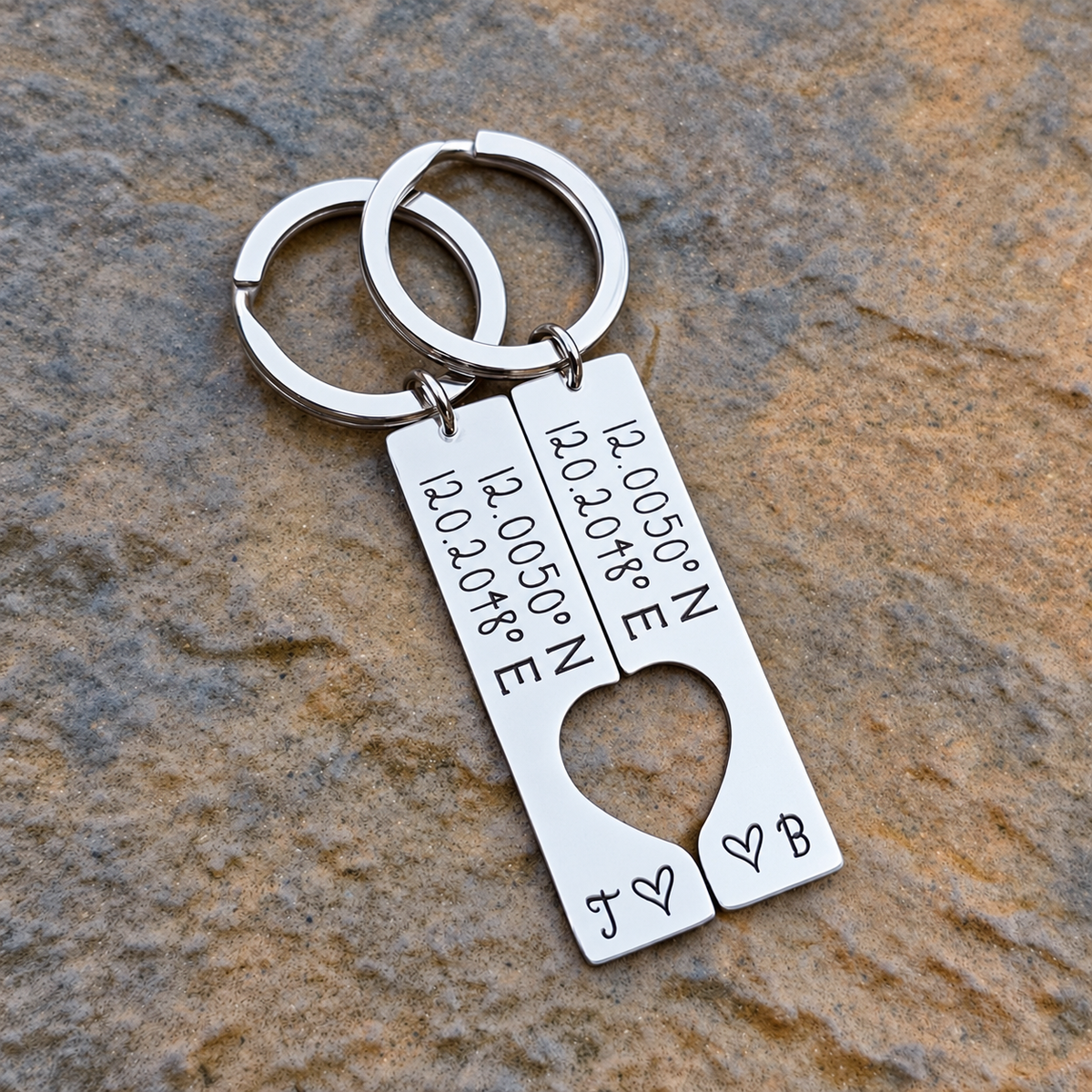 Overhead view of two stainless steel coordinates keyrings placed together on stone to form a heart-shaped cut-out, with initials J and B
