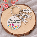 Personalised This Auntie Is Loved By aluminium keyring with colourful flowers, a butterfly and charms named Maisie, Oakley and Jake on a wood slice
