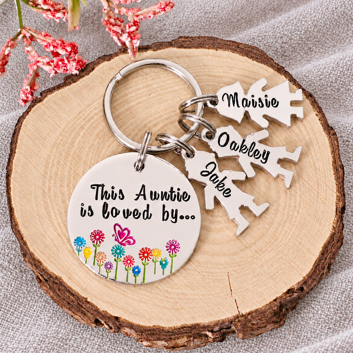 Personalised This Auntie Is Loved By aluminium keyring with colourful flowers, a butterfly and charms named Maisie, Oakley and Jake on a wood slice
