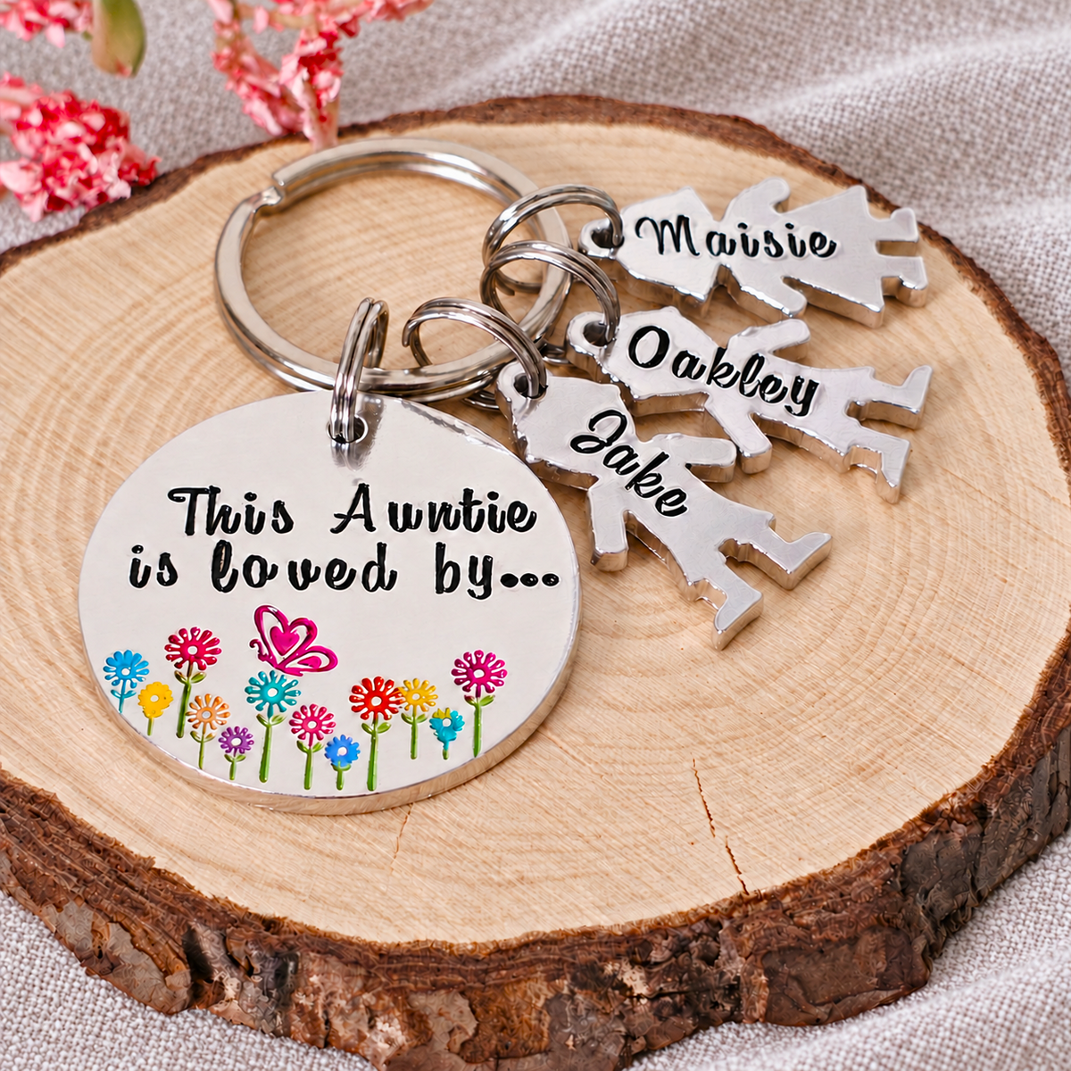 Angled close-up of a floral This Auntie Is Loved By keyring with Maisie, Oakley and Jake little people charms on wood
