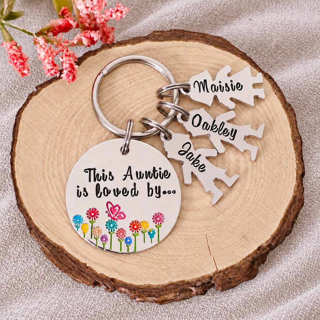 Personalised Auntie keyring with three named little people charms displayed on a wood slice beside pink flowers
