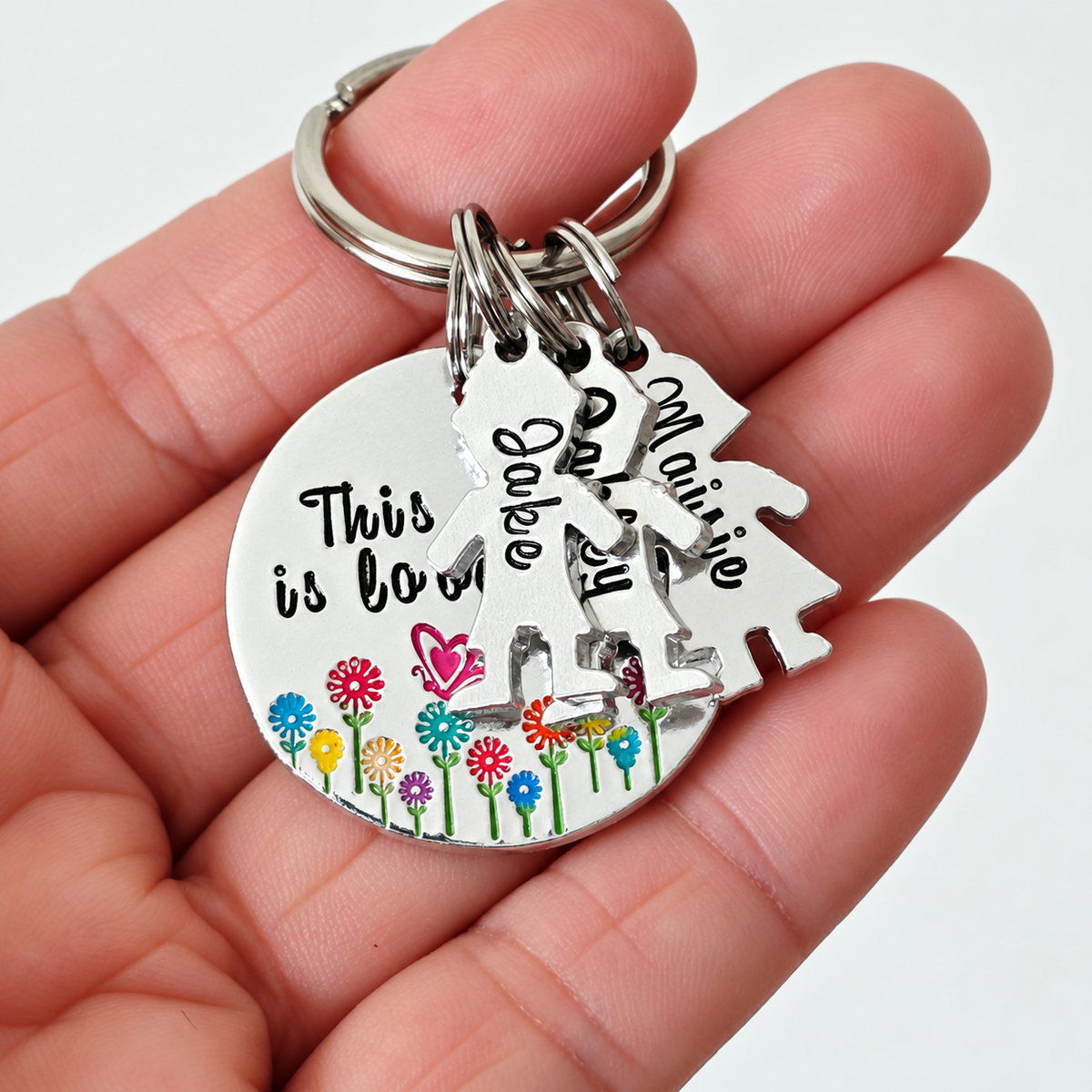 Auntie little people keyring resting on a hand, showing named charms and a colourful flower and butterfly design
