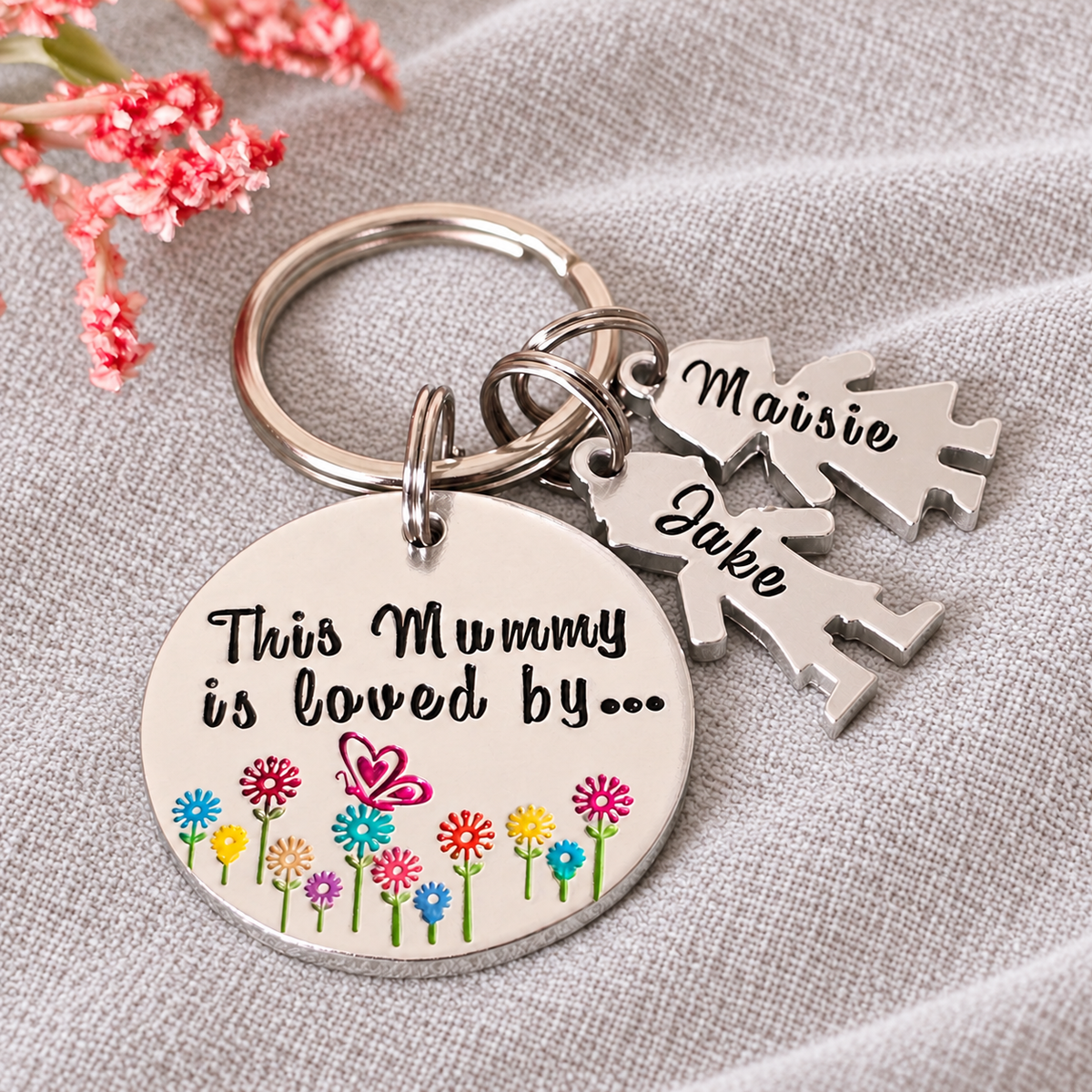 Close-up of a personalised Mummy keyring with colourful stamped flowers, a butterfly and Maisie and Jake little people charms
