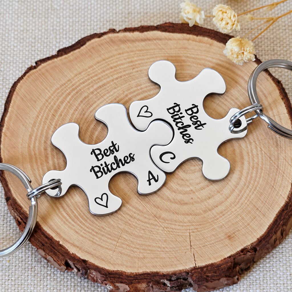 Matching Best Bitches puzzle keyrings with engraved initials and hearts beside dried flowers

