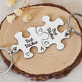 Two interlocking stainless steel Best Bitches puzzle keyrings engraved with initials A and C and outline hearts on a wood slice
