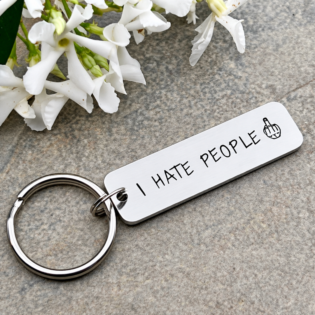 Close-up of an aluminium I Hate People keyring showing the stamped lettering and middle finger symbol
