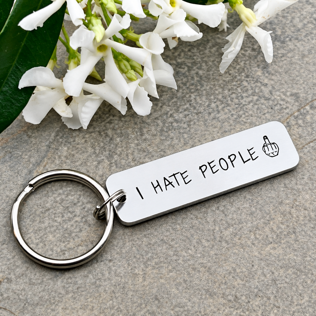Rectangular I Hate People keyring displayed beneath white flowers with its split ring to the left
