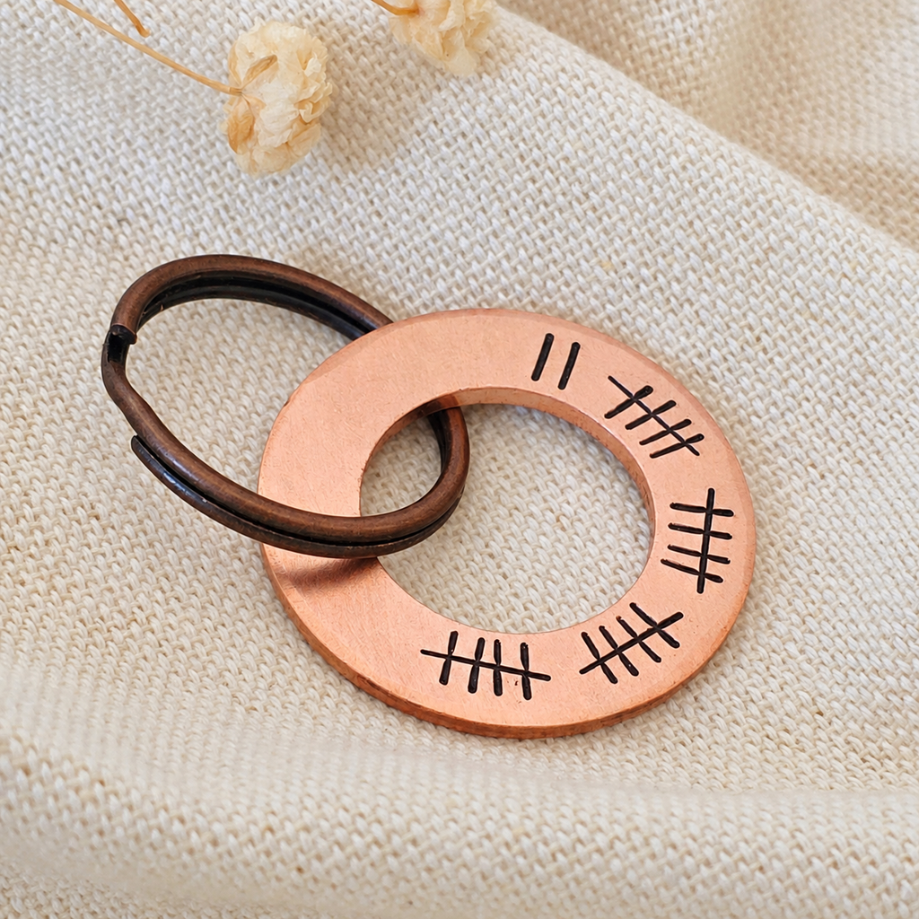 Angled close-up of a copper washer keyring with 22 tally marks and a dark split ring on linen fabric
