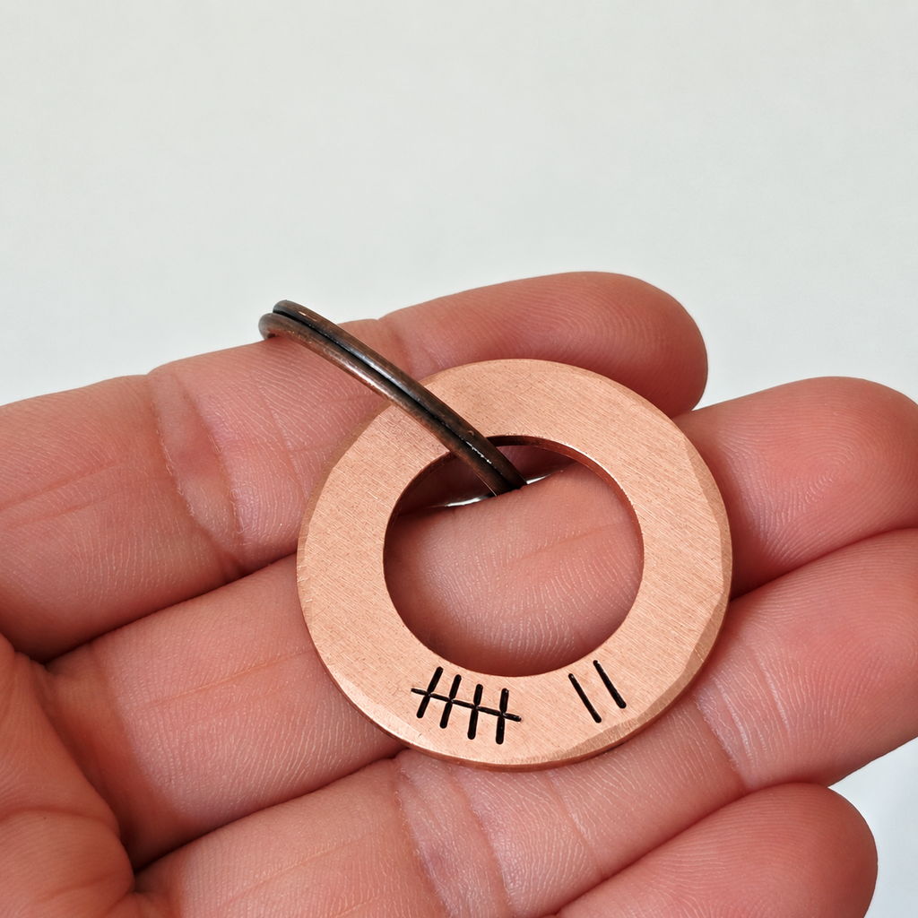 Copper 7th anniversary washer keyring held in a hand, showing the open-centred design and seven tally marks
