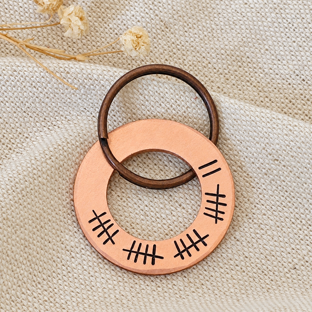 Front view of a copper 22nd anniversary tally keyring on folded linen fabric with dried flowers
