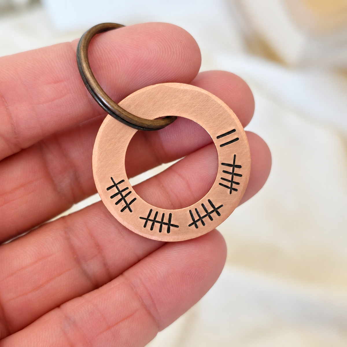 Copper washer keyring held in a hand, showing 22 hand stamped tally marks around the open-centred tag
