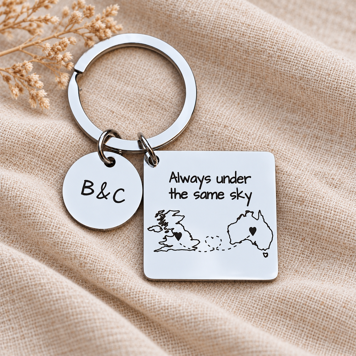 Personalised steel map keyring with UK and Australia outlines, Always under the same sky wording and a B&C initials charm on cream linen
