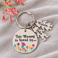 Personalised This Mummy Is Loved By aluminium keyring with colourful flowers, a butterfly and little people charms named Maisie and Jake on linen
