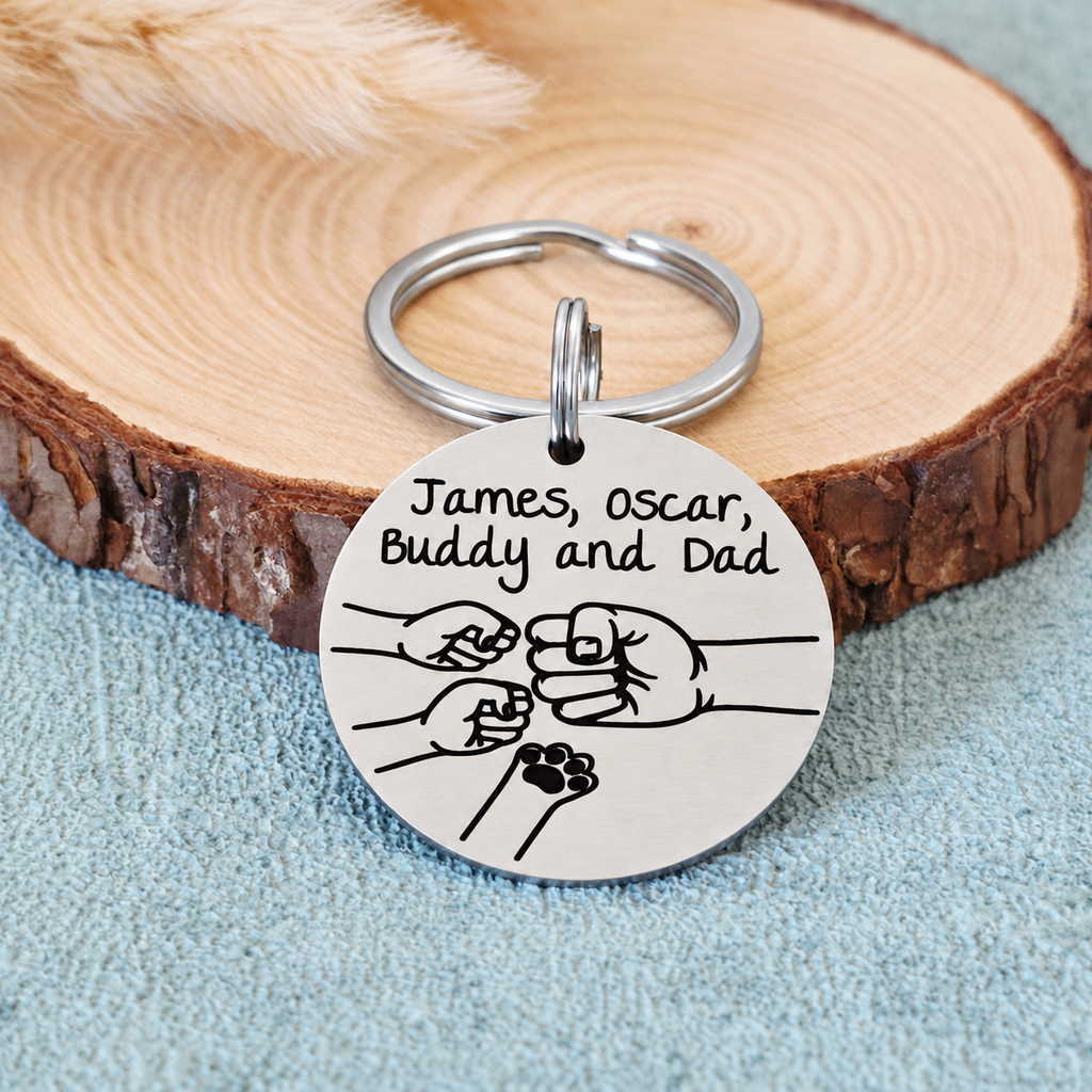 Personalised stainless steel Dad fist bump keyring with family names, two small fists and a pet paw, displayed against a wood slice
