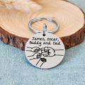 Personalised stainless steel Dad fist bump keyring with family names, two small fists and a pet paw, displayed against a wood slice
