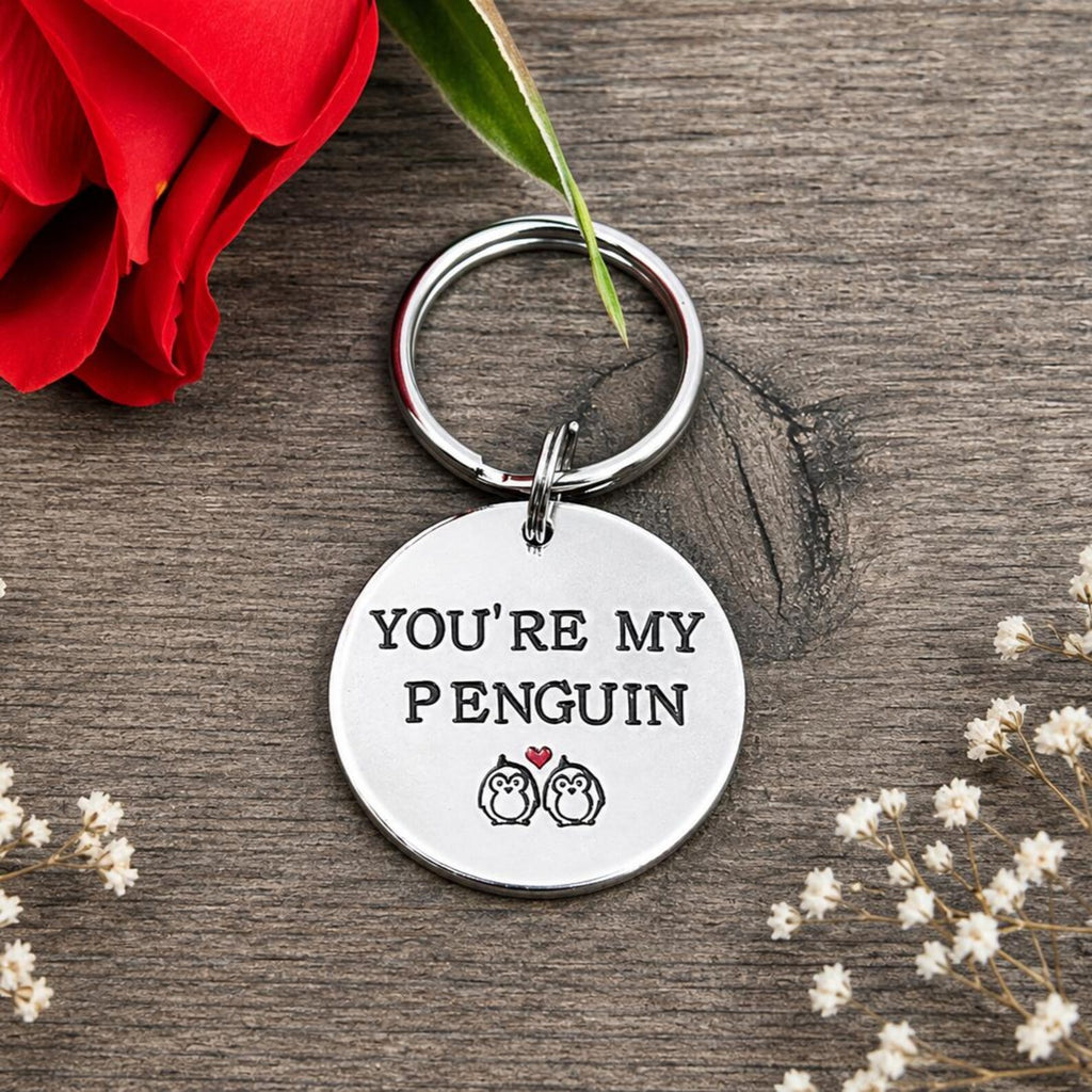 Personalised You're My Penguin keyring displayed beneath a red rose and framed by small dried white flowers
