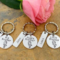 Three personalised brother keyrings arranged beneath a pink rose, with round wording tags and rectangular name tags
